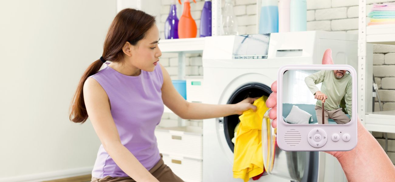 Woman using a washing machine with a small screen displaying a video of an elderly man under her care.